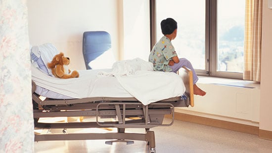 病院 & 外科センター－病院のベッドに座って窓の外を見つめている男の子