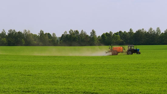 Ammonia fertilizer dispensing machine pulled by a tractor across an open field with vibrant grass and trees in the distance.