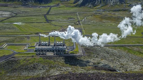 Large geothermal power plant with several pipes expanding outward through a valley.